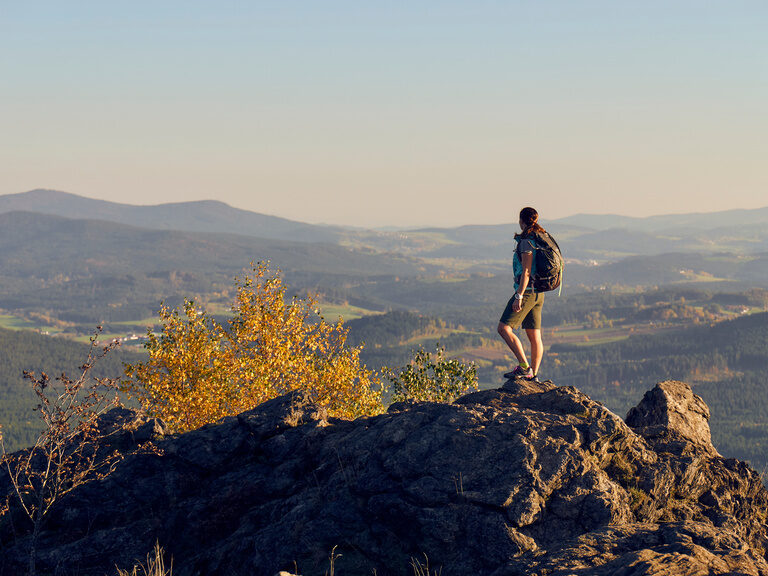 Ein Wanderer steht auf einem Felsen und hat einen majestätischen Ausblick auf den Bayerischen Wald